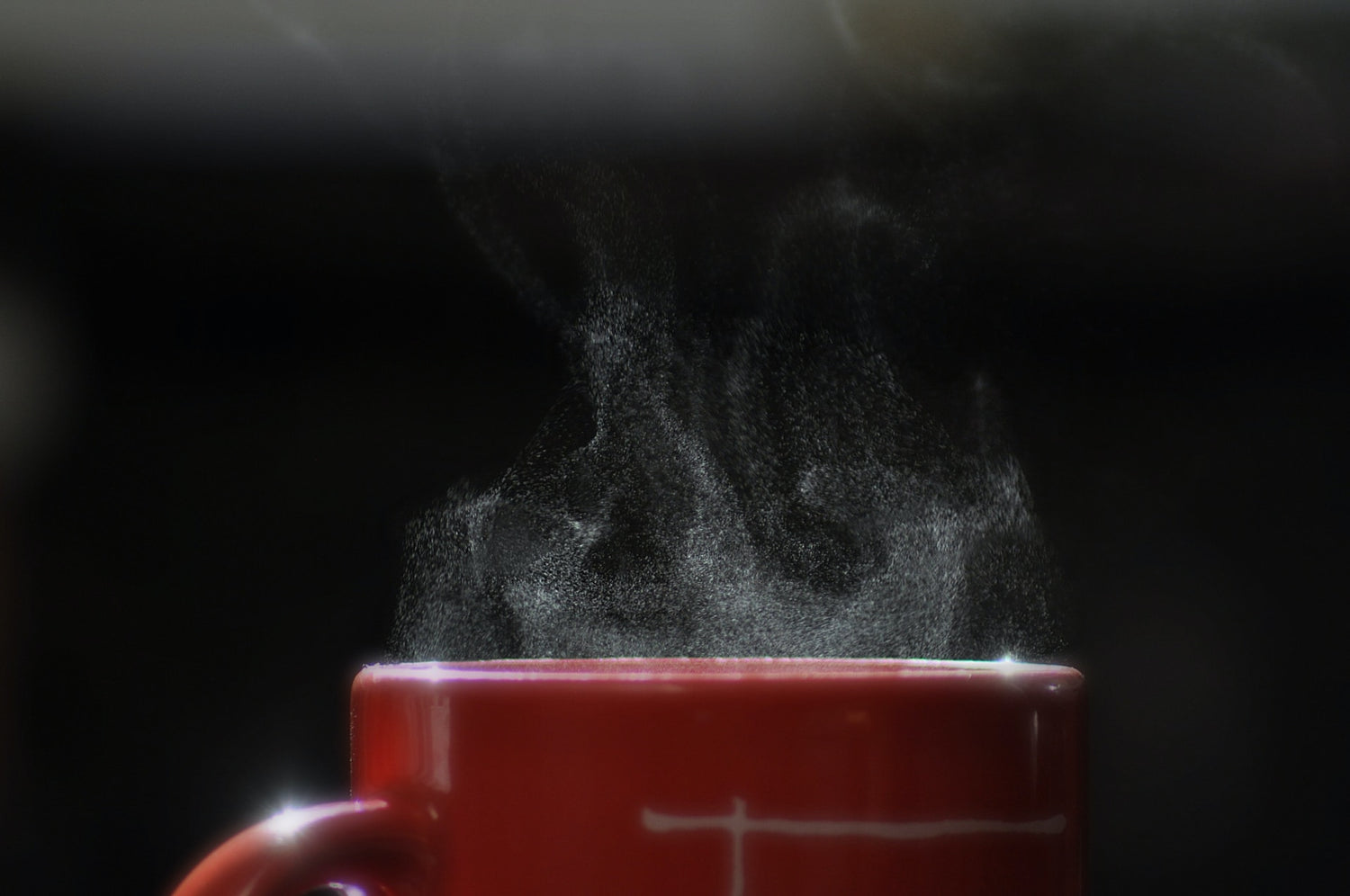 Tasse rouge laissant entrevoir une fumé blanche sur fond noir